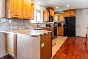 Kitchen with stainless steel appliances, a peninsula, wood finish cabinets, recessed lighting, and dark stone countertops