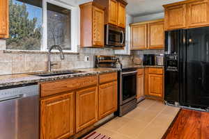 Kitchen featuring stainless steel appliances, dark stone counters, wood finish cabinetry, light tile patterned flooring, and decorative backsplash