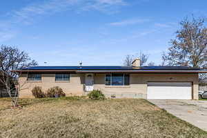 Ranch-style house featuring brick siding, a front yard, roof mounted solar panels, and concrete driveway