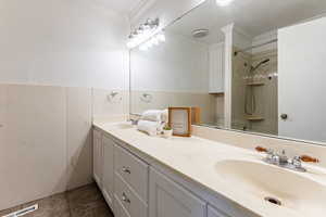 Full bathroom featuring double vanity, ornamental molding, a wainscoted wall, and shower / bathtub combination