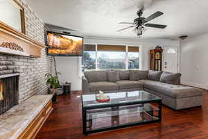 Living room featuring a brick fireplace, dark wood finished floors, a ceiling fan, and a textured ceiling