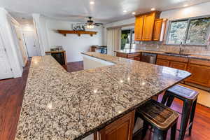 Kitchen with dark wood-style floors, wood finish cabinetry, tasteful backsplash, a kitchen breakfast bar, and recessed lighting
