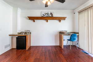 Bar featuring dark wood-type flooring, ceiling fan, black fridge, ornamental molding, and dark stone countertops