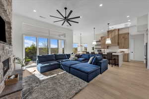 Living area with light wood finished floors, ceiling fan, hanging lights, a fireplace, and a high ceiling