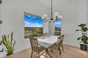 Dining space with light wood-style floors, lofted ceiling, and suspended lighting
