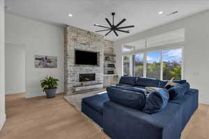 Living room featuring light wood finished floors, ceiling fan, a stone fireplace, and recessed lighting