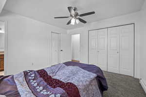 Carpeted bedroom with baseboard heating, ceiling fan, multiple closets, connected bathroom, and a textured ceiling