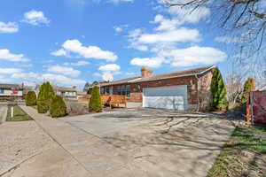 Single story home featuring concrete driveway, brick siding, a garage, and a chimney
