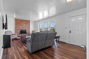 Living room featuring a textured ceiling, dark wood-style flooring, a fireplace, and a baseboard heating unit