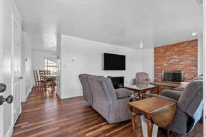 Living room featuring a brick fireplace, wood finished floors, and a textured ceiling