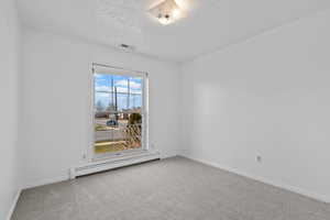 Unfurnished room featuring a baseboard heating unit, light colored carpet, and a textured ceiling