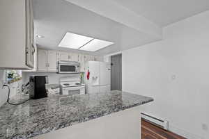 Kitchen featuring a baseboard heating unit, white appliances, a skylight, a peninsula, and dark wood-style floors