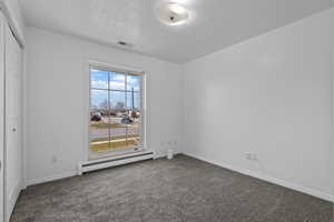 Unfurnished room with a baseboard heating unit, dark colored carpet, and a textured ceiling