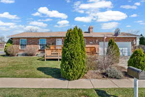 Single story home featuring brick siding, a garage, a wooden deck, a front lawn, and a chimney