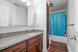 Full bath featuring vanity, shower / tub combo with curtain, dark wood-type flooring, a baseboard radiator, and a textured ceiling