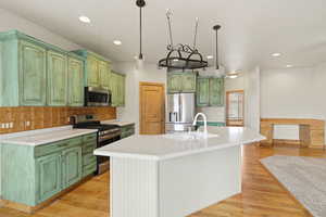 Kitchen featuring stainless steel appliances, light countertops, an island with sink, decorative backsplash, and light wood finished floors