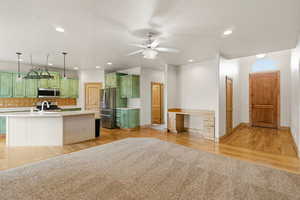 Dual tone kitchen with tasteful backsplash, an island with sink, a ceiling fan, light wood-style floors, and recessed lighting