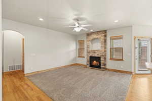 Unfurnished living room featuring arched walkways, a ceiling fan, light wood finished floors, a fireplace, and recessed lighting
