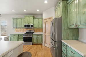 Kitchen with green cabinetry, stainless steel appliances, light countertops, and recessed lighting