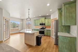 Kitchen featuring green cabinetry, a kitchen island with sink, stainless steel appliances, light countertops, and tasteful backsplash