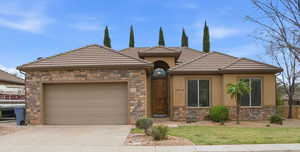 View of front of property with an attached garage, stone siding, concrete driveway, and a tiled roof