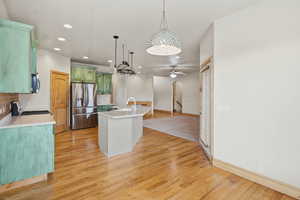 Kitchen with green cabinetry, stainless steel appliances, a center island with sink, light wood-type flooring, and arched walkways