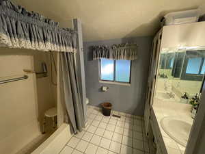 Full bathroom with double vanity, a textured ceiling, a shower stall, and light tile patterned floors