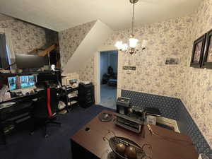 Office area featuring wallpapered walls, hanging lights, dark carpet, and a textured ceiling