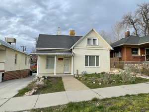 View of front of property with a porch, brick siding, roof with shingles, and a chimney
