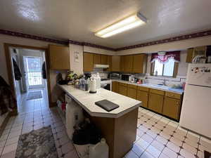 Kitchen with white appliances, wood finish cabinetry, a textured ceiling, a peninsula, and tile countertops