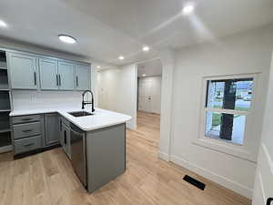 Kitchen featuring a peninsula, gray cabinetry, light stone countertops, light wood-style flooring, and recessed lighting