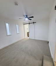 Unfurnished bedroom with a barn door, a ceiling fan, carpet floors, and connected bathroom