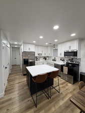 Remodeled Kitchen featuring two tone color scheme, stainless steel appliances, backsplash, light wood-type flooring, and a breakfast bar