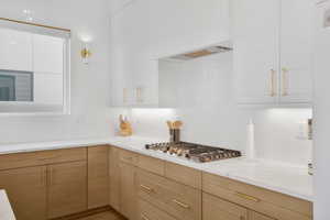 Kitchen featuring light stone counters, stainless steel gas cooktop, white cabinetry, and wood finished floors