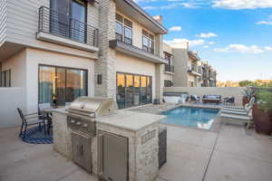 View of pool with an outdoor kitchen with living area, a hot tub, a balcony, and patio surround