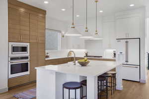 Dual tone kitchen with white appliances, an island with sink, light wood-style flooring, light stone counters, and dual tone cabinetry