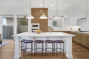 Kitchen with dual tone cabinets, light wood-type flooring, hanging light fixtures, light stone counters, and a breakfast bar