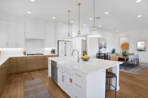 Two tone kitchen featuring two tone color scheme, tasteful backsplash, light wood-type flooring, light stone counters, and decorative light fixtures