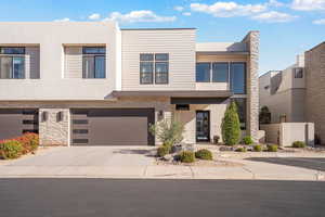 Contemporary house featuring stone siding, stucco siding, a garage, and concrete driveway