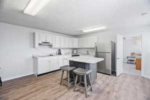 Downstairs: two tone kitchen with freestanding refrigerator, a breakfast bar, a kitchen island, light wood-style flooring, and dual tone cabinetry