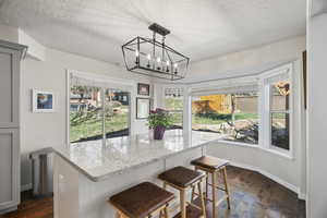 Kitchen with light stone countertops, a kitchen island, dark wood finished floors, a kitchen bar, and a textured ceiling