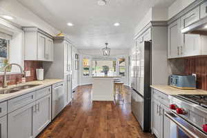 Kitchen with light stone countertops, dark wood-style floors, gray cabinets, stainless steel appliances, and tasteful backsplash