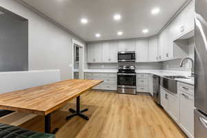 Kitchen with stainless steel appliances, light wood-style floors, recessed lighting, and white cabinets