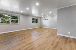 Empty room with light wood-type flooring, crown molding, hanging lights, and a textured ceiling