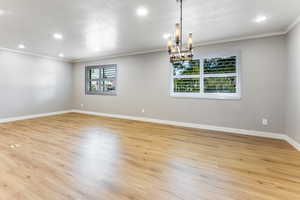 Spare room featuring a chandelier, crown molding, and light wood-type flooring