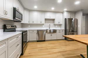 Kitchen with stainless steel appliances, light wood-style flooring, recessed lighting, butcher block countertops, and white cabinetry