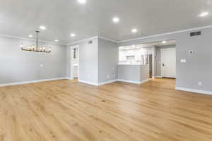 Unfurnished living room featuring light wood-type flooring, crown molding, and a chandelier