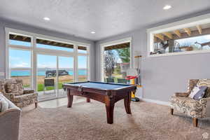 Recreation room featuring a water view, billiards table, light colored carpet, a textured ceiling, and recessed lighting