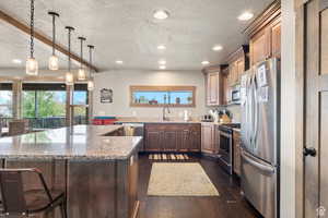 Kitchen featuring stainless steel appliances, a textured ceiling, light stone counters, beam ceiling, and dark wood-type flooring