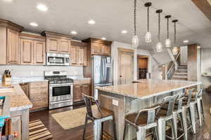 Kitchen featuring light stone countertops, stainless steel appliances, pendant lighting, a spacious island, and dark wood-style floors